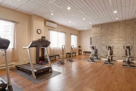 Exercise room with treadmills and stationary bicycles beside curtained windows