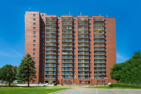 Tall brick apartment building with balconies, lawn and parking spaces