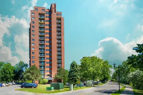 Tall brick building beside trees, a lawn and a curved roadway