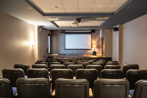 Cinema room with rows of seats and a projection screen.