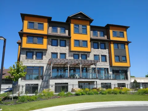 Building with yellow panels, grey stone walls, a glass-railed terrace and a lawn