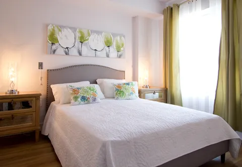 Bedroom with a white bed, bedside lamps, wooden furniture and wall art