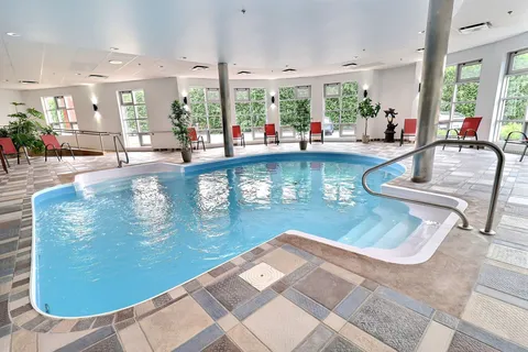 Indoor swimming pool with handrails and chairs beside tall windows