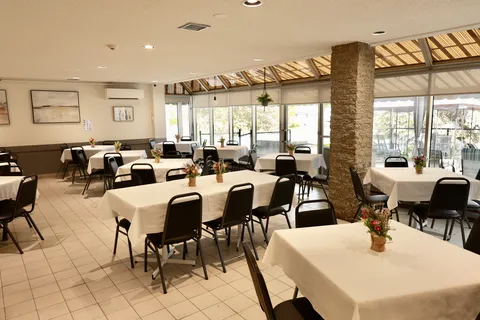 Dining room with tablecloths, dark chairs and a glass-walled seating area