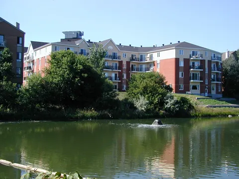 Residence buildings beside a pond and trees.