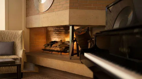 Grand piano beside a brick fireplace and lounge seating.