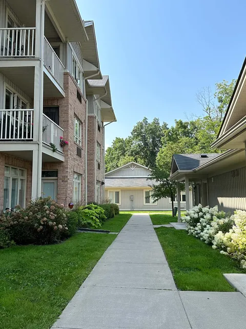 Path between a brick residence and low villas, with white flowers and trees