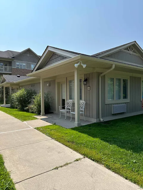 Single-storey villa with a covered porch, two white chairs and a paved path
