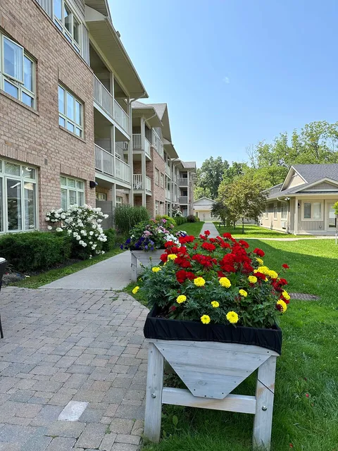 Raised flower planters beside a lawn and path, with brick buildings behind
