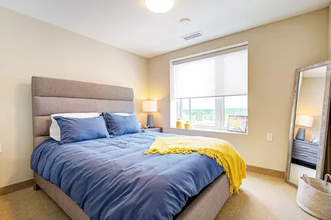 Bedroom with blue bedding, a yellow throw, a bedside lamp and a tall mirror