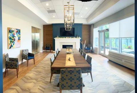 Room with a long dining table, blue chairs, tall windows and a fireplace