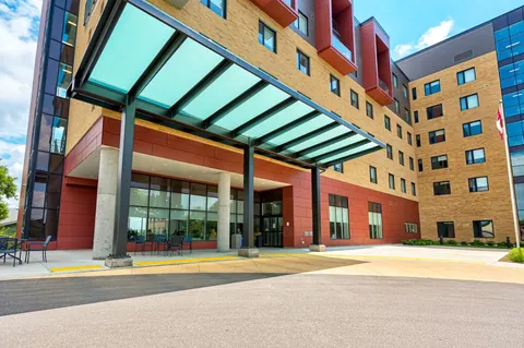 Glass-covered entrance beneath a brick facade with chairs along the windows