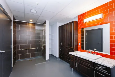Bathroom with an orange tiled wall, sink, glass shower enclosure and dark cupboards