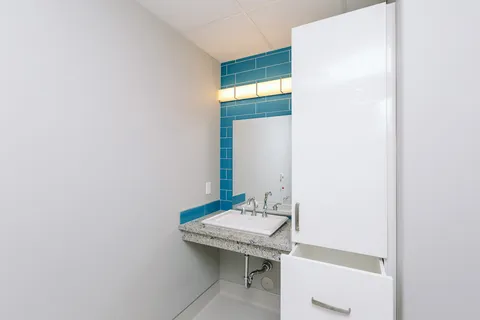 Bathroom with a sink, white cupboards and a blue tiled wall