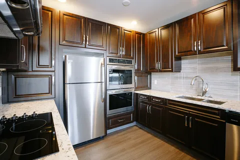 Kitchen with dark cupboards, a refrigerator, ovens, cooktop and sink