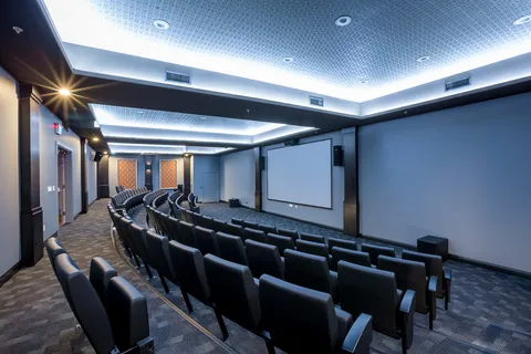 Theatre room with rows of upholstered seats and a blank screen