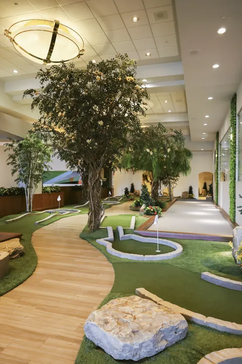 Indoor miniature golf course with artificial turf, rocks, a wooden path and trees