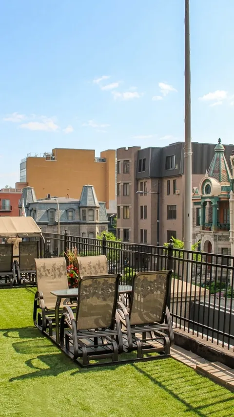 Terrace with patio chairs, a table, flowers and a metal railing beside neighbouring buildings