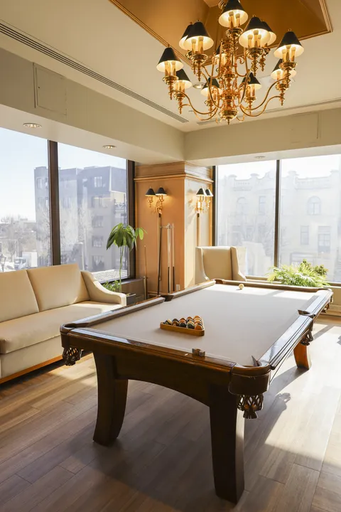 Billiards room with a pool table, sofa, armchair, chandelier and large windows