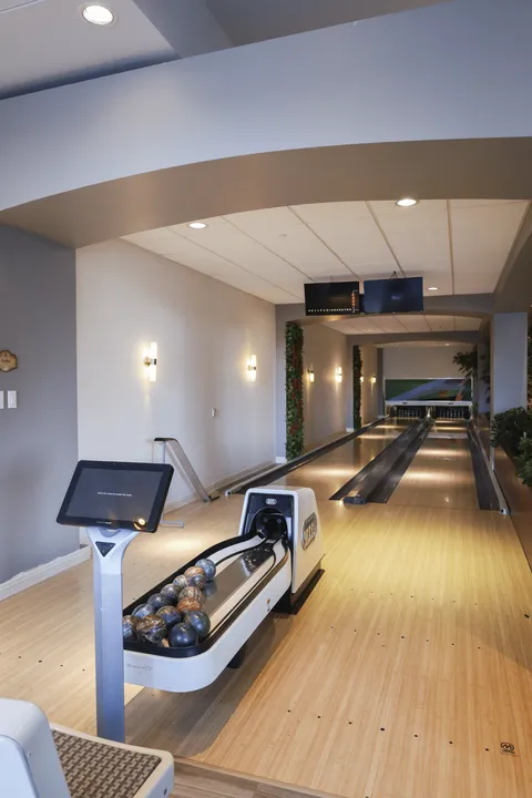 Bowling lanes with a ball return, touchscreen, scoring monitors and potted plants