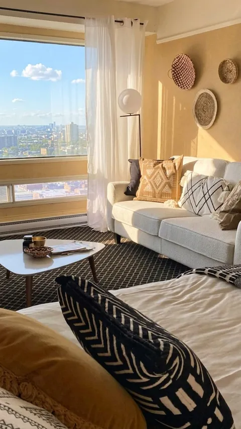 Room with a bed, white sofa, floor lamp, woven wall decorations and a large window