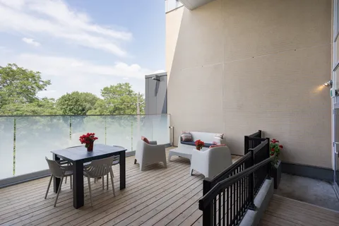 Deck with white chairs, a table, potted red flowers and glass railings
