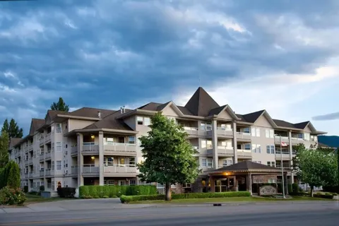 Apartment building with balconies, trees and a covered entrance.