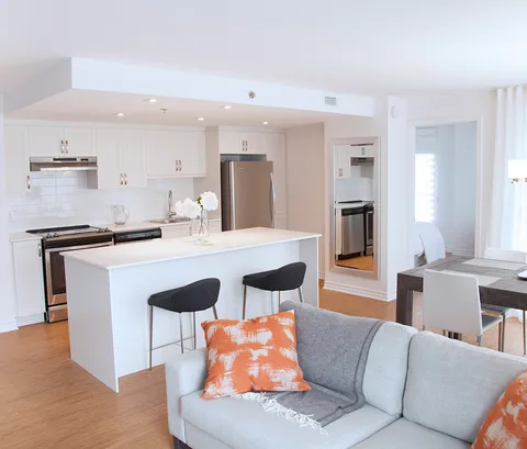 White kitchen with an island and stools beside a grey sofa and dining table