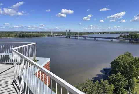 Balcony with white railings overlooking trees, a river and a bridge