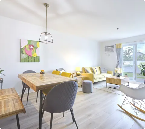 Suite living and dining area with yellow sofa and large windows.