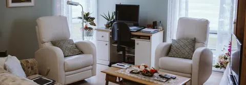 Apartment sitting area with white armchairs, a desk and a television.