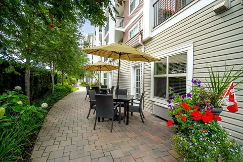Paved garden path with patio tables, yellow umbrellas and flower beds