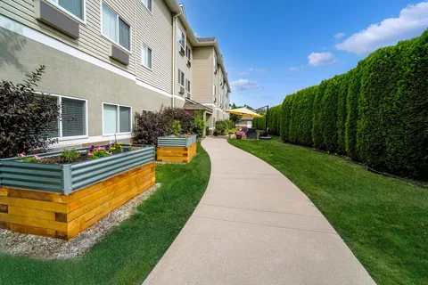 Side of the residence beside a paved path, raised planters and hedges