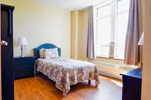 Bedroom with a single bed, dark furniture and a large curtained window