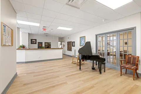 Open room with a grand piano, wooden chair, reception counter and glass doors