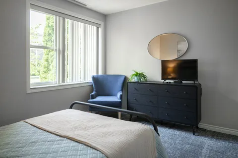 Bedroom with a bed, armchair, dresser, television and window