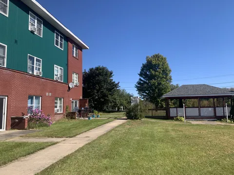 Residence building beside a lawn, paved path and gazebo.