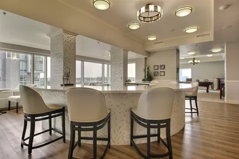 Room with bar stools around a white counter and large windows