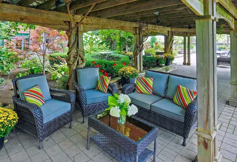 Patio seating beneath a wooden pergola beside garden beds.