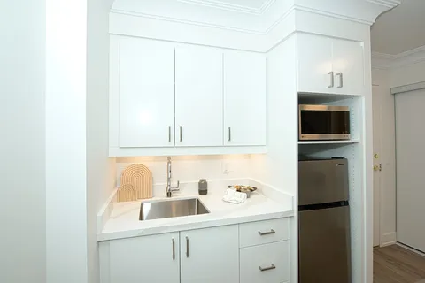 White kitchenette with cabinets, sink, refrigerator and microwave.