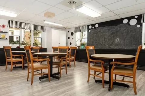 Room with round tables, wooden chairs, a large chalkboard and striped window valances