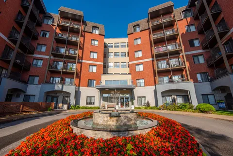 Red-brick residence with balconies, an entrance canopy and a fountain surrounded by flowers