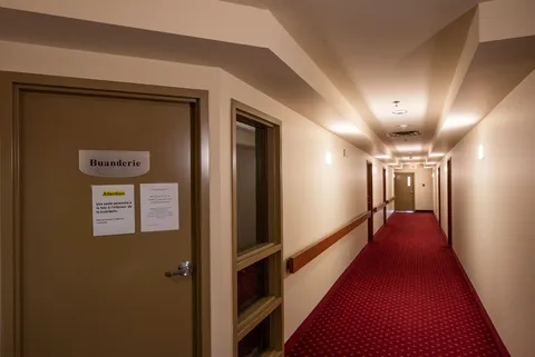 Corridor with red carpeting, cream walls, doors and handrails