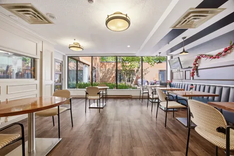 Café seating area with round tables, chairs, a bench and large windows.