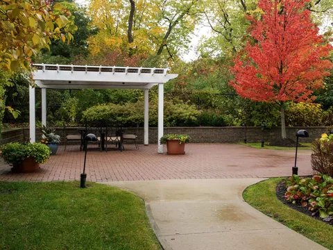 Patio with a white pergola, tables and trees in autumn colours