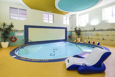 Indoor exercise pool with handrails and poolside equipment.