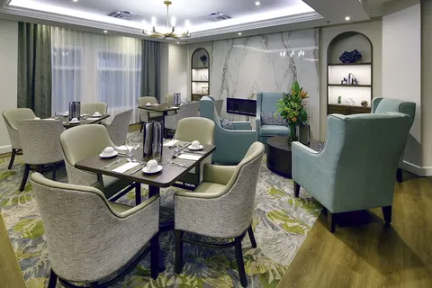 Dining area with set tables, upholstered chairs and large windows.