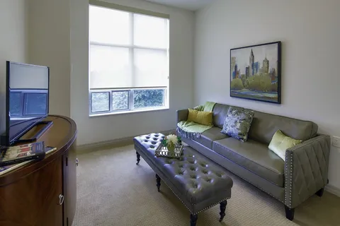 Suite living room with a sofa, television and tufted ottoman.