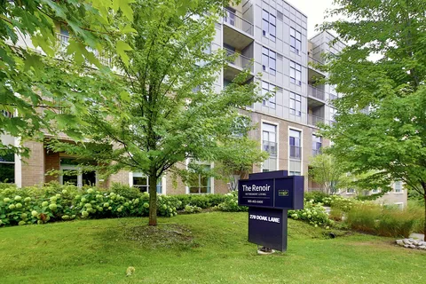 Residence building with balconies behind trees and its entrance sign.