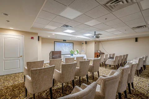 Rows of chairs facing a table, piano and projection screen